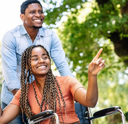 An african american woman in a wheelchair enjoying a walk outdoors  with her daughter and husband.